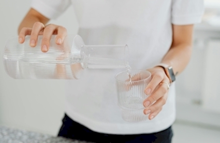 Person gießt Wasser in ein Glas